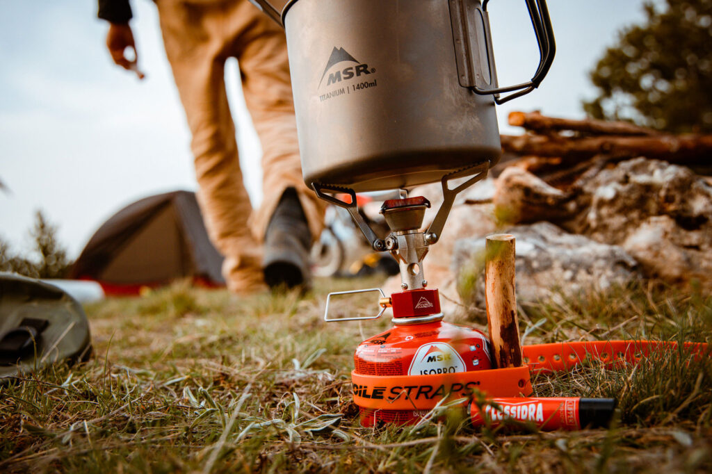 Voile Strap in a camp setting holding a rocket stove upright during use.
