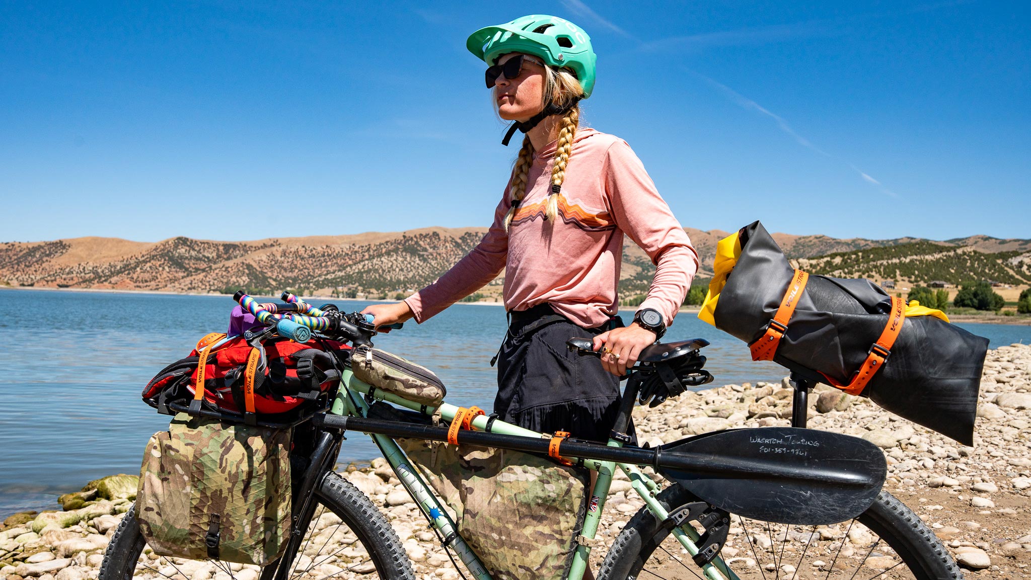 Bikepacker with Voile Straps and Voile Rack Straps securing a packraft and paddles to bike for transport.